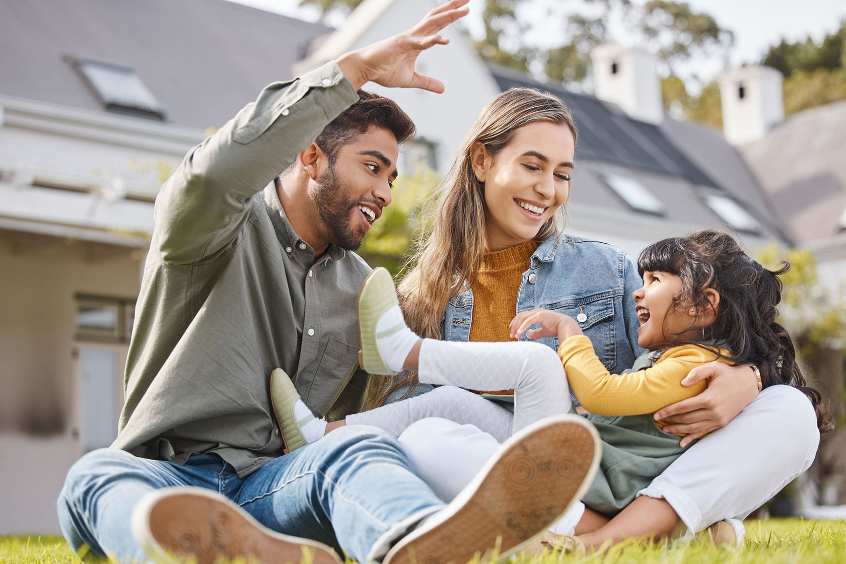 Two adults and a child playing in the grass in a yard.