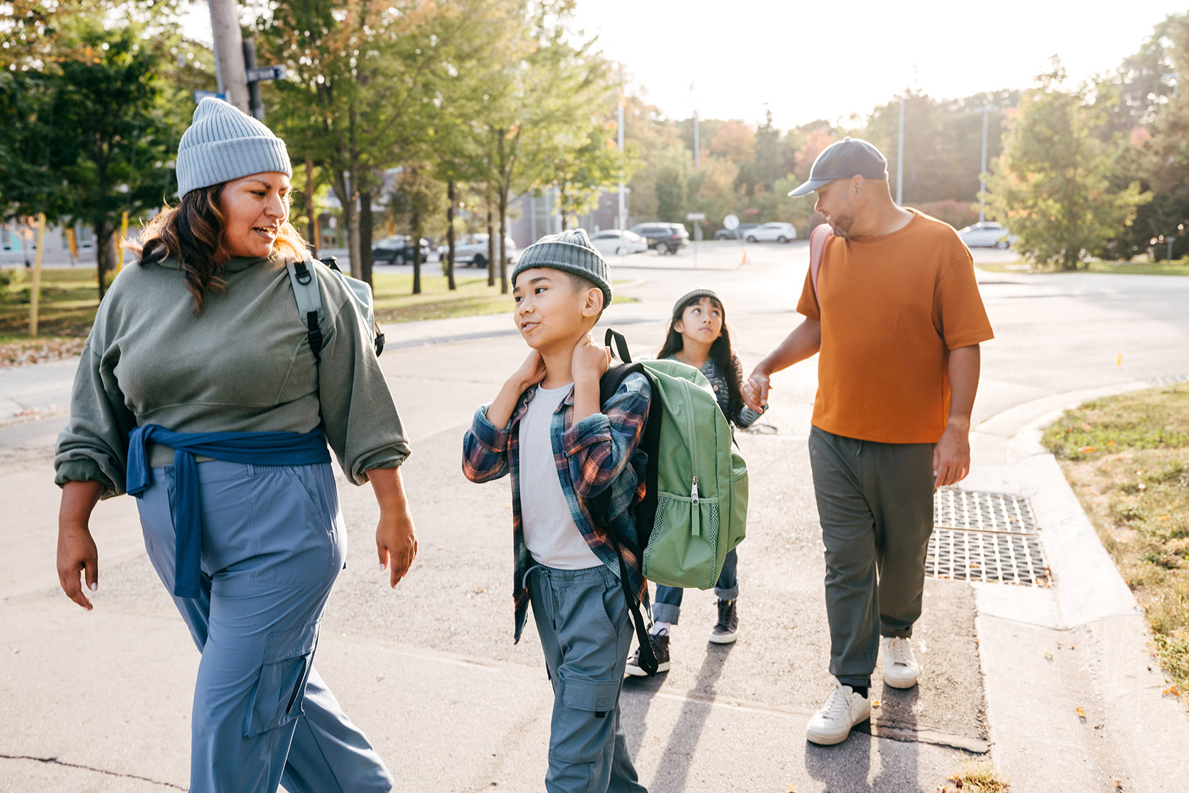 Two parents and two kids walking on the street with backpacks.