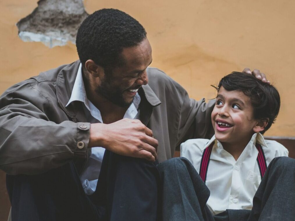 Man sits next to smiling boy with soccer ball.